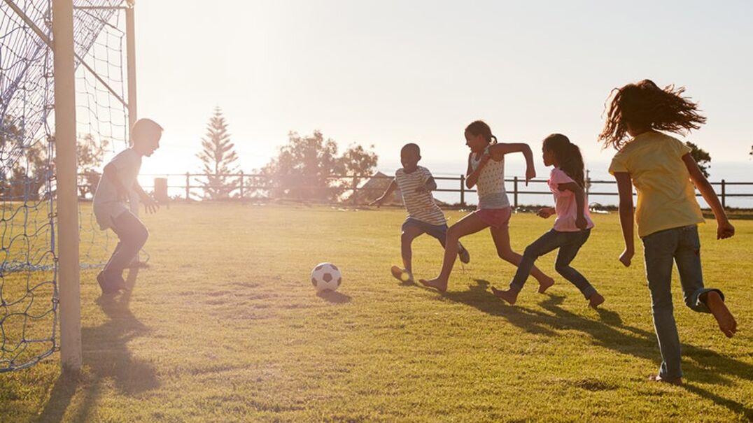 A group of five children outside playing soccer