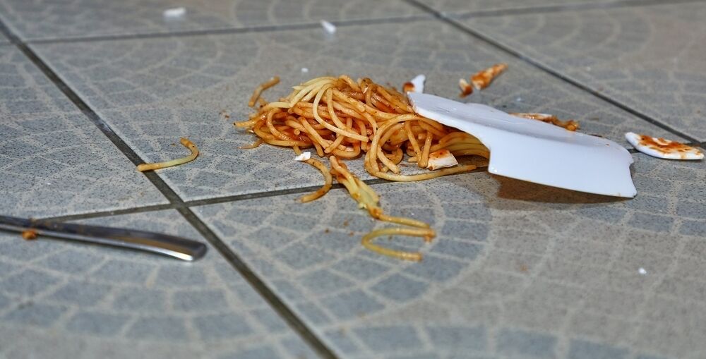 A smashed plate of spaghetti with napoli sauce and a fork on blue tiles.