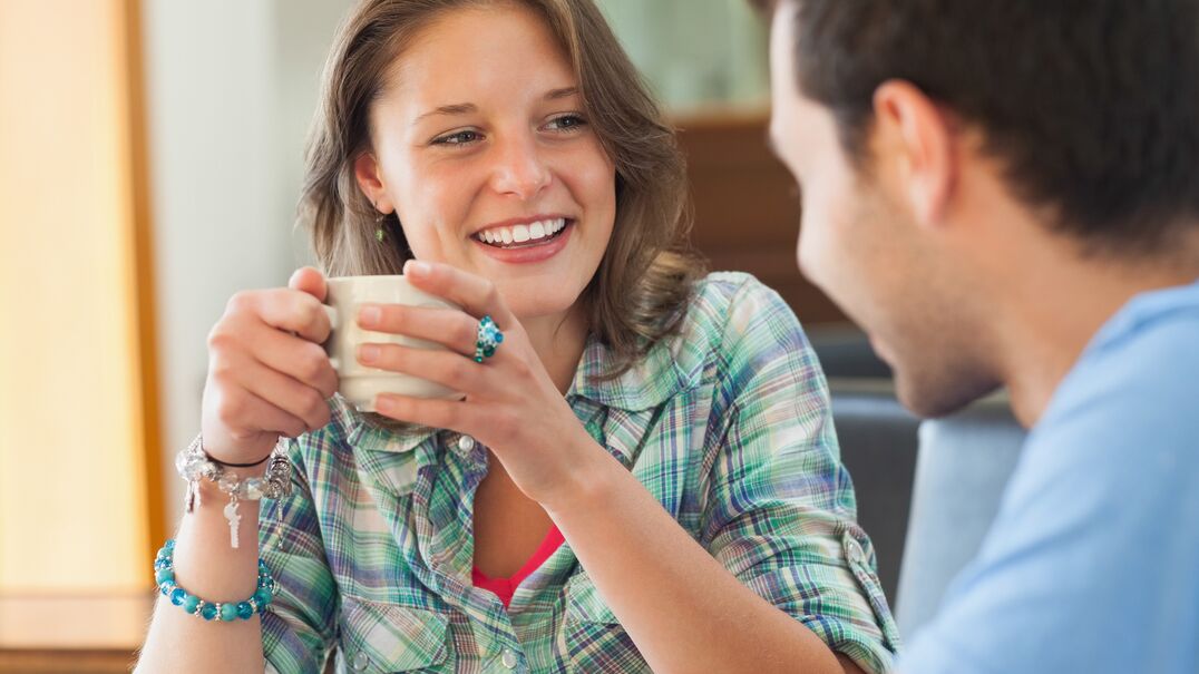 Lady smiling with cup of tea talking to a man